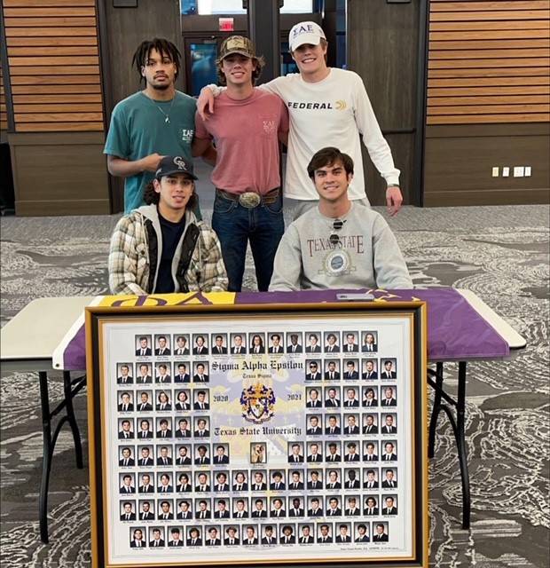 Five men of Sigma Alpha Epsilon pose behind a table that features their organization's composite photo