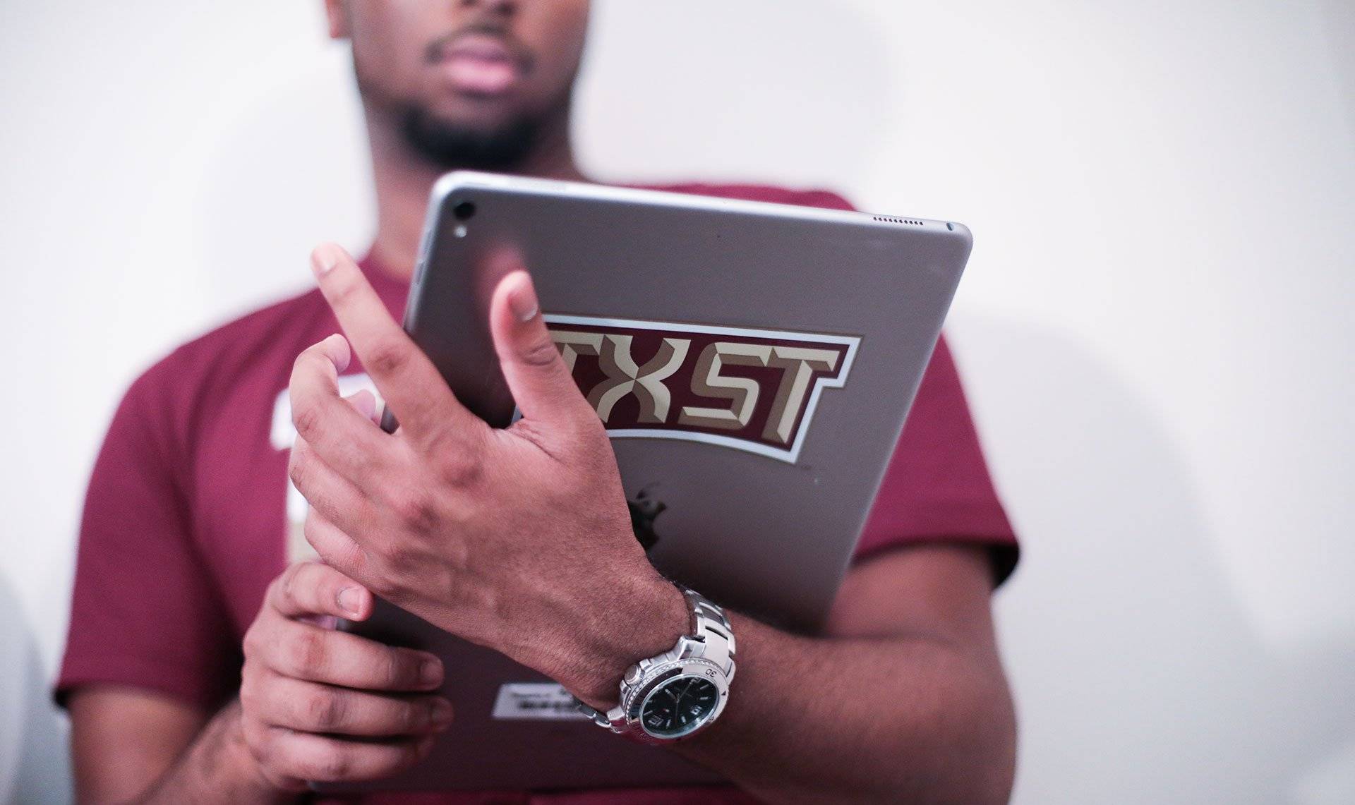 A students holds an ipad with a TXST sticker on the back.