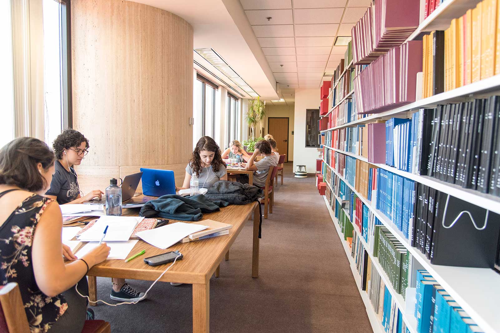 students study at a table beside a colorful book shelf