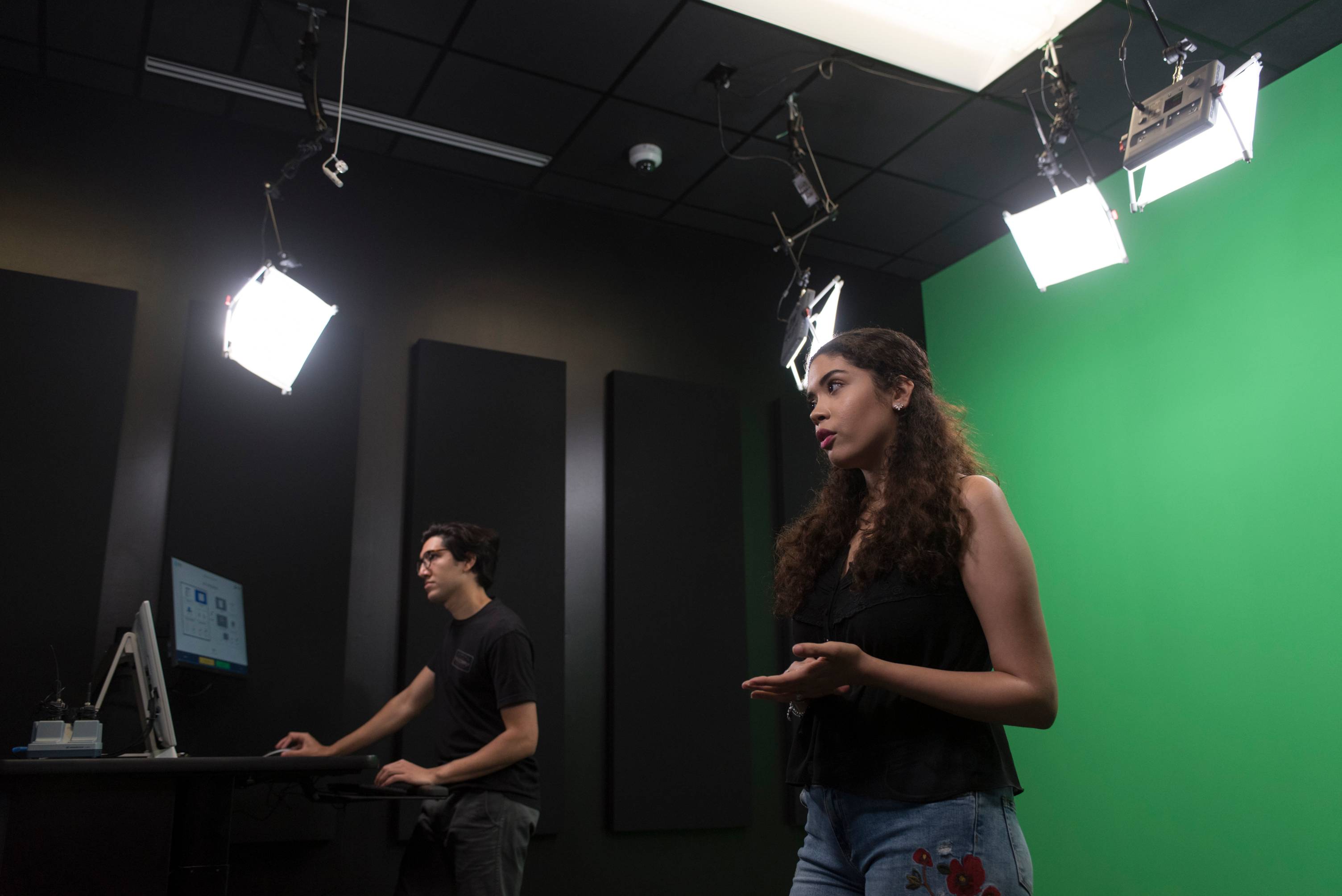 Woman in studio lighting and green screen background and man operating computer