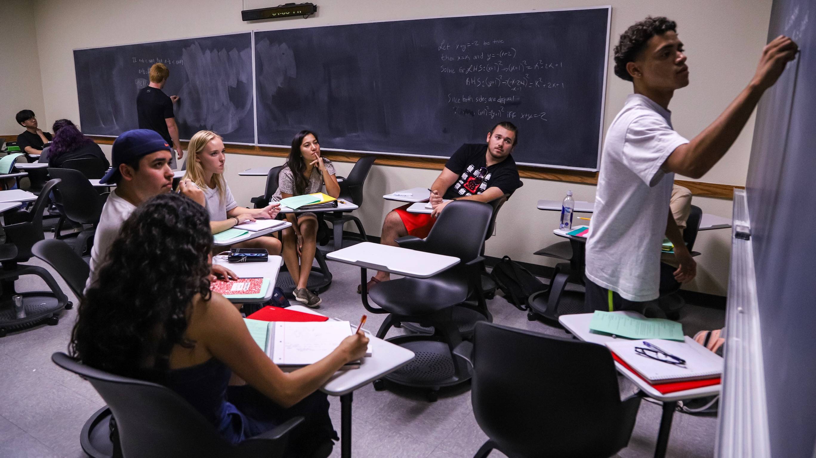 Student in a classroom working on the board with fellow students looking on.