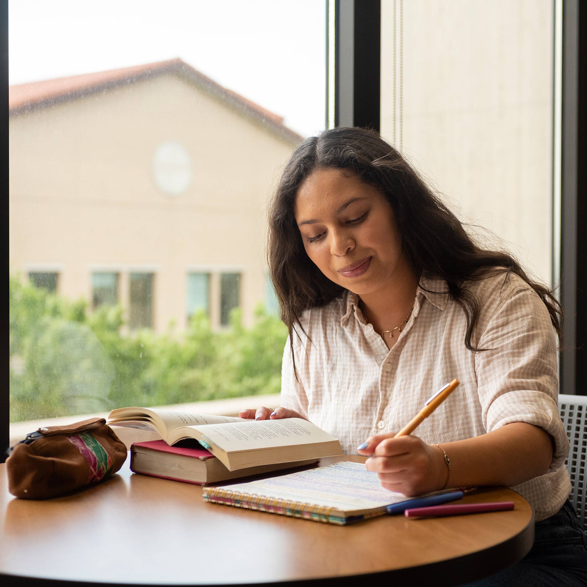 Accounting student reading textbook and taking notes near window