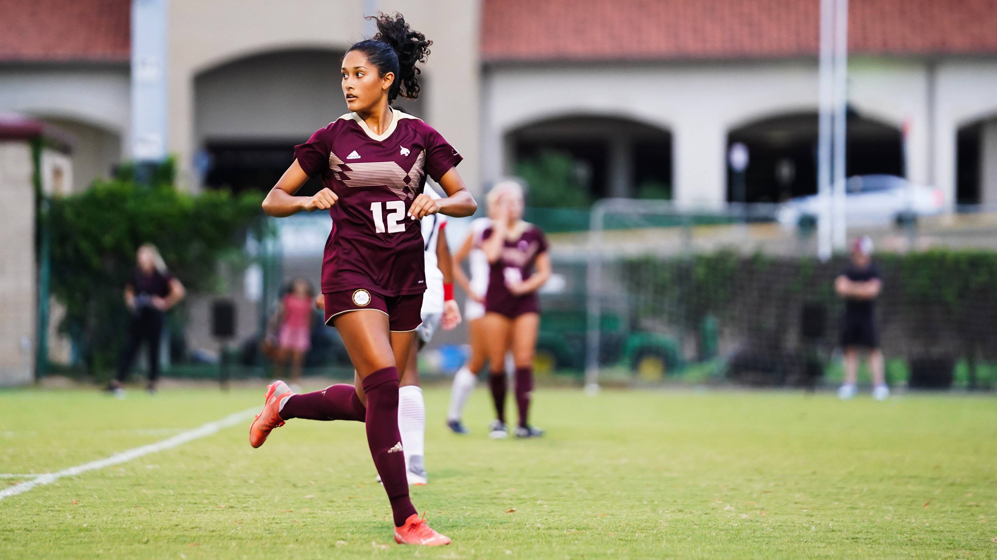 Juana Plata running on soccer pitch and looking back wearing maroon Texas State soccer uniform