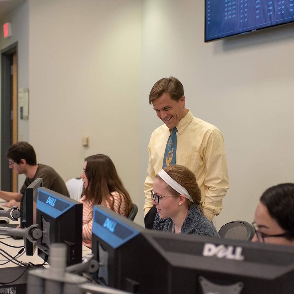 Professor working with students in trading lab