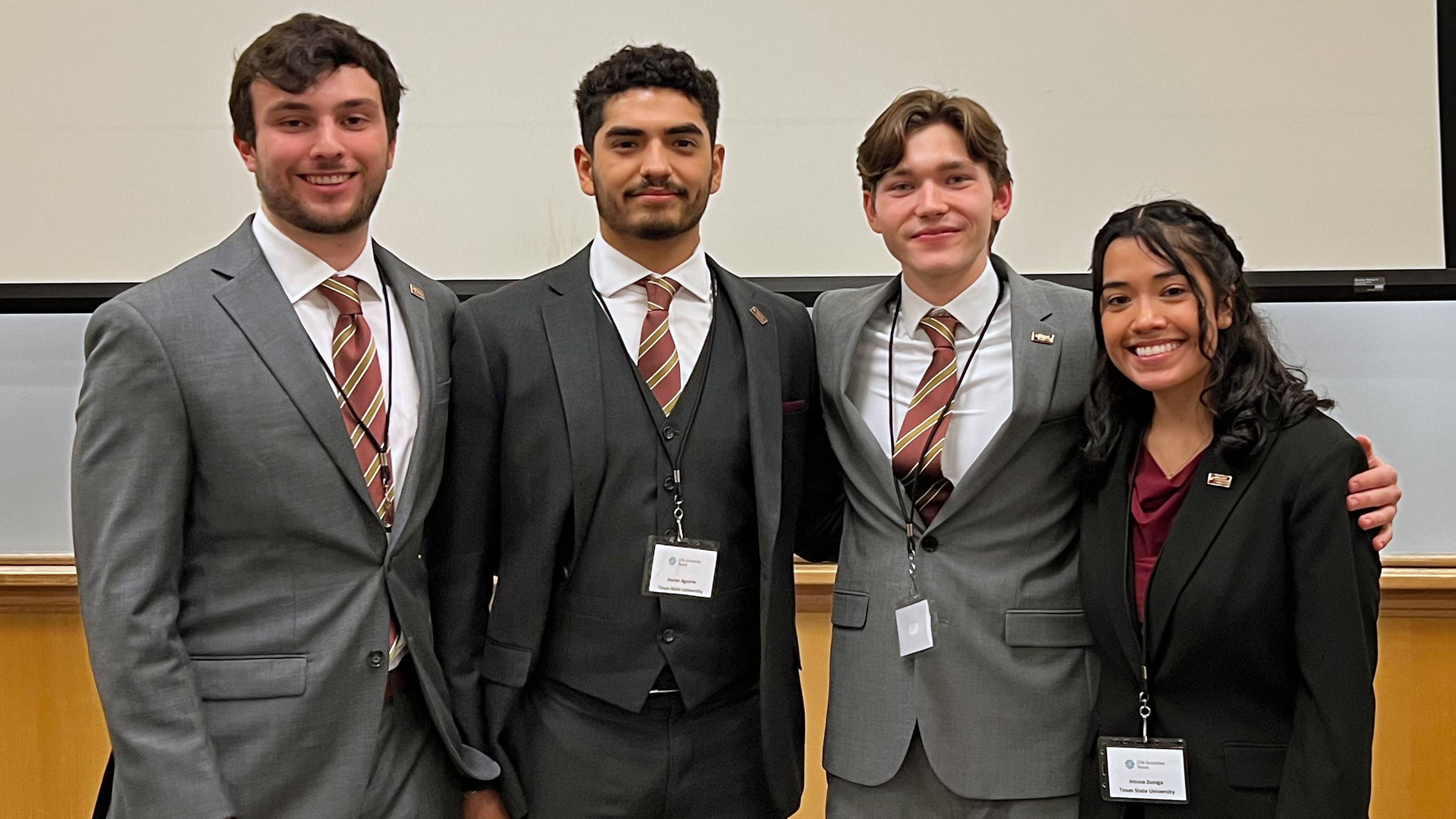Four college students in business attire smiling and posing indoors.