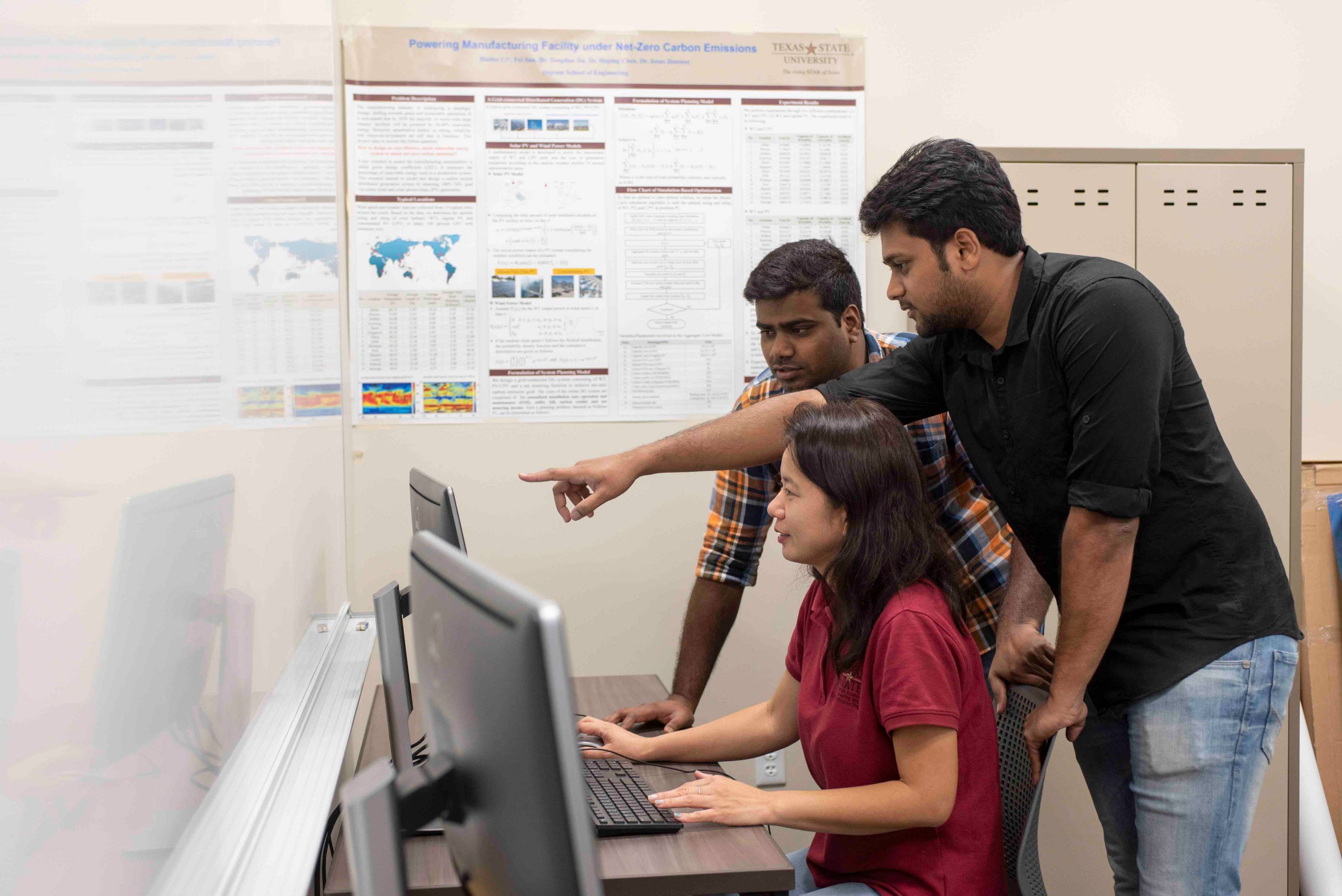 Person using computer with two colleagues looking over work