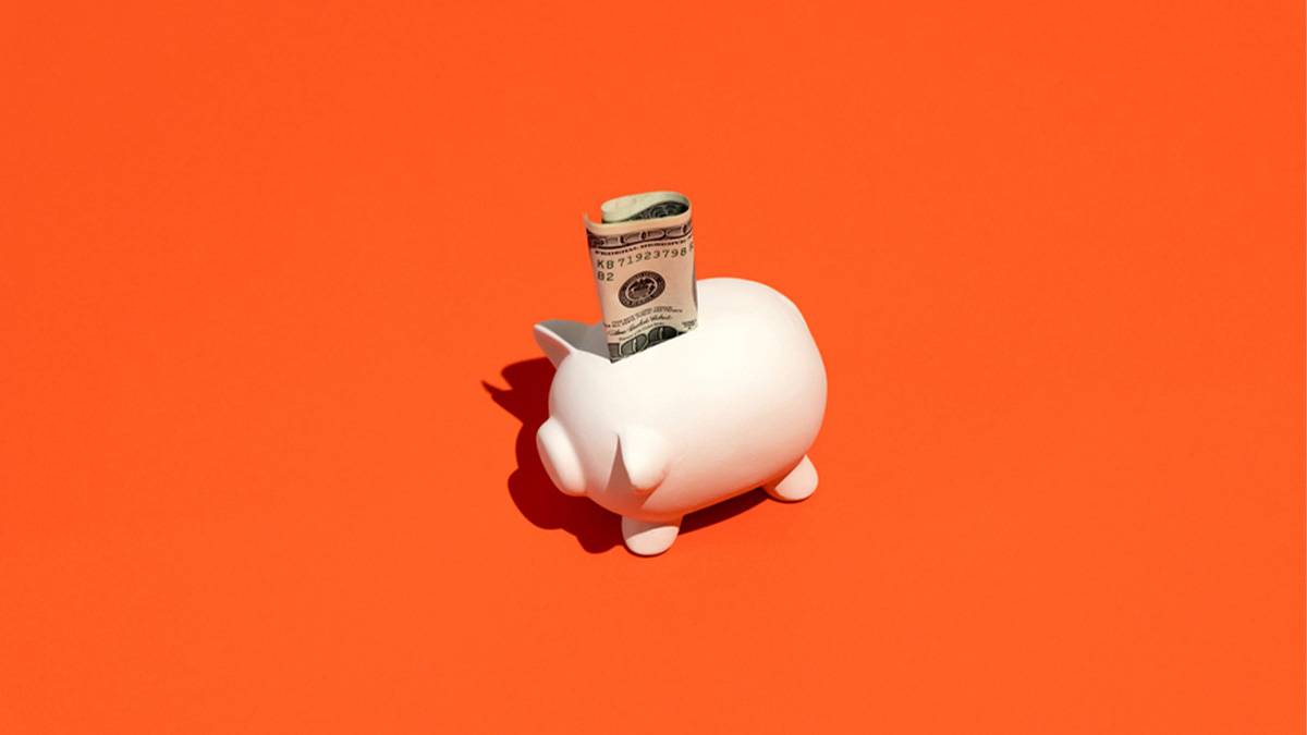 Piggy bank with cash in the slot on a orange backdrop