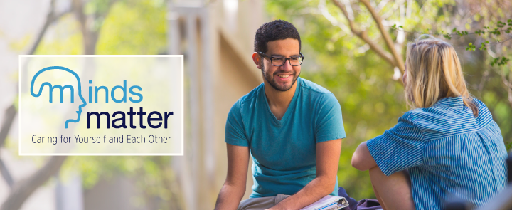 Two students talking to each other with Minds Matter logo. “minds matter" text is in two different shades of blue. The initial “m” spreads into an outline of a human head. The “m” in the head depicts a brain.