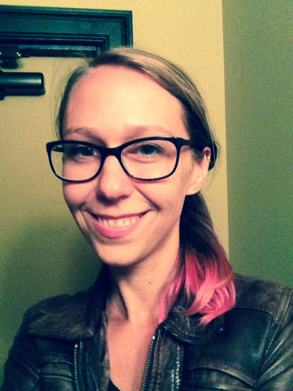 Woman with dyed hair wearing glasses in front of wall