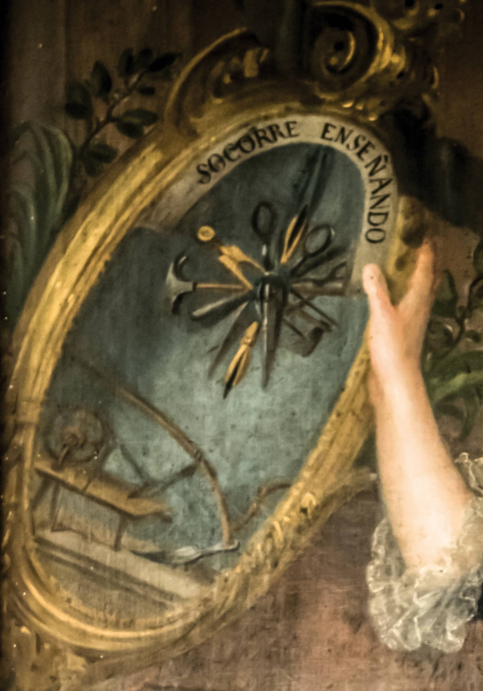 Painting of woman's arm in front of another large round painting with the words "socorre enseñando" in Spanish on it