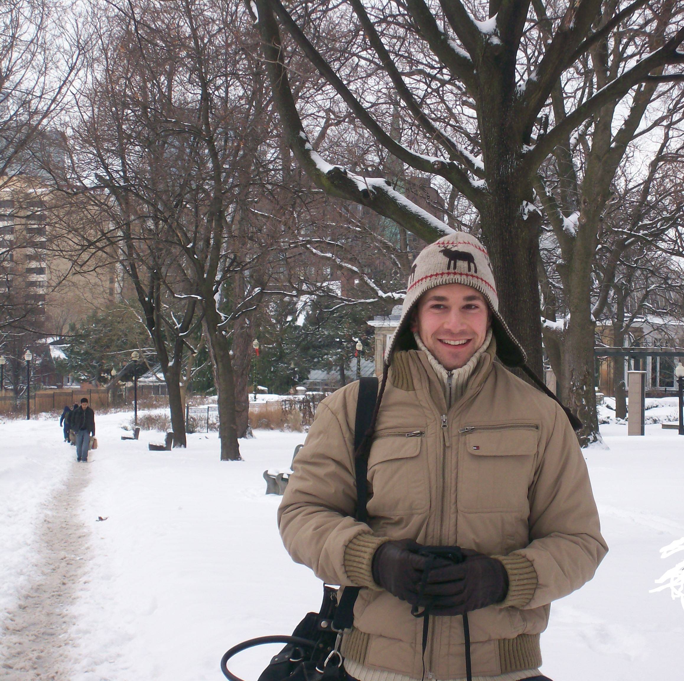 Man wearing anorak and gloves with a shoulder bag in snow, trees