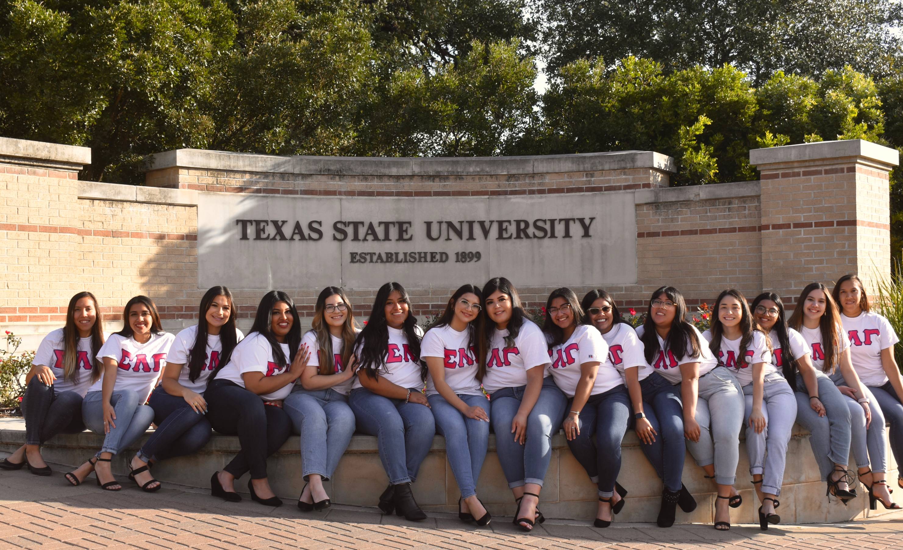 Women of Sigma Lambda Gamma wearing matching organization shirts and posing in front of a Texas State University sign