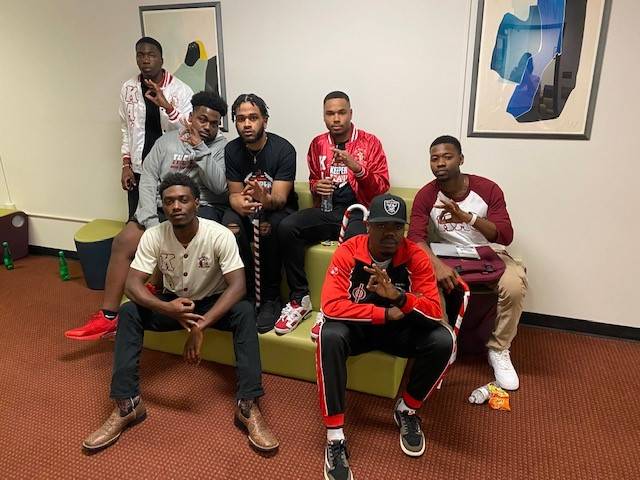 Men of Kappa Alpha Psi congregated in the LBJ Student Center and holding up their organization's hand signs