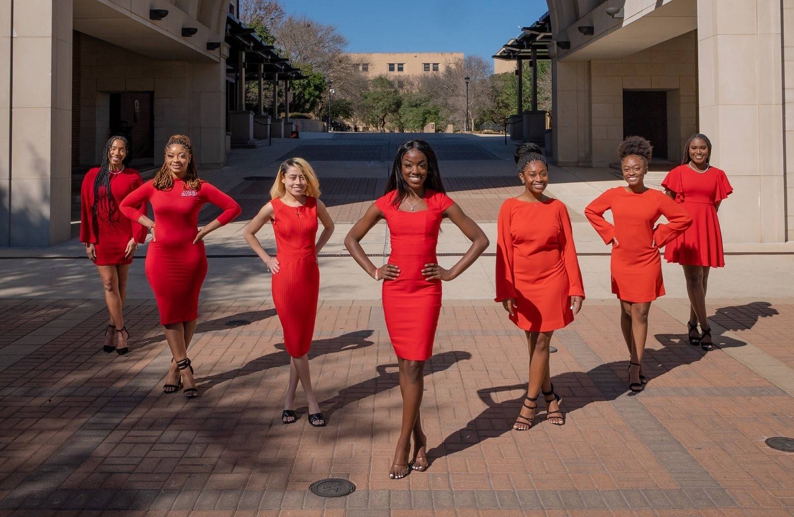 Women of Delta Sigma Theta standing in a V formation on campus wearing matching red dresses