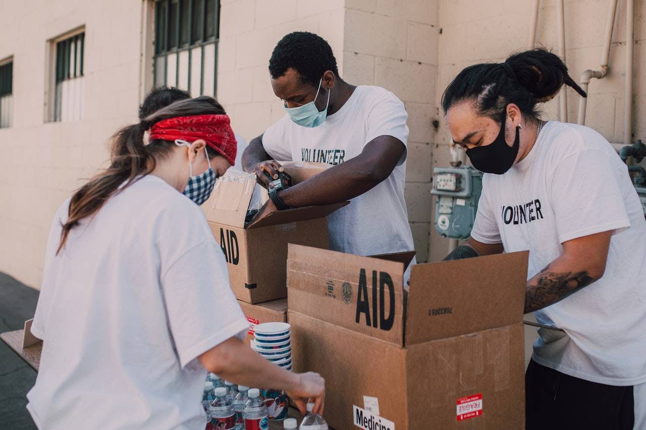 three volunteering loading food items into cardboard boxes