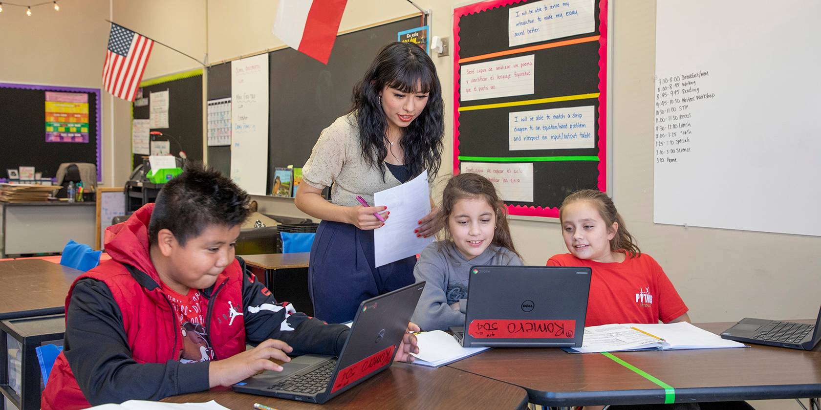 teacher helping 3 young students with schoolwork