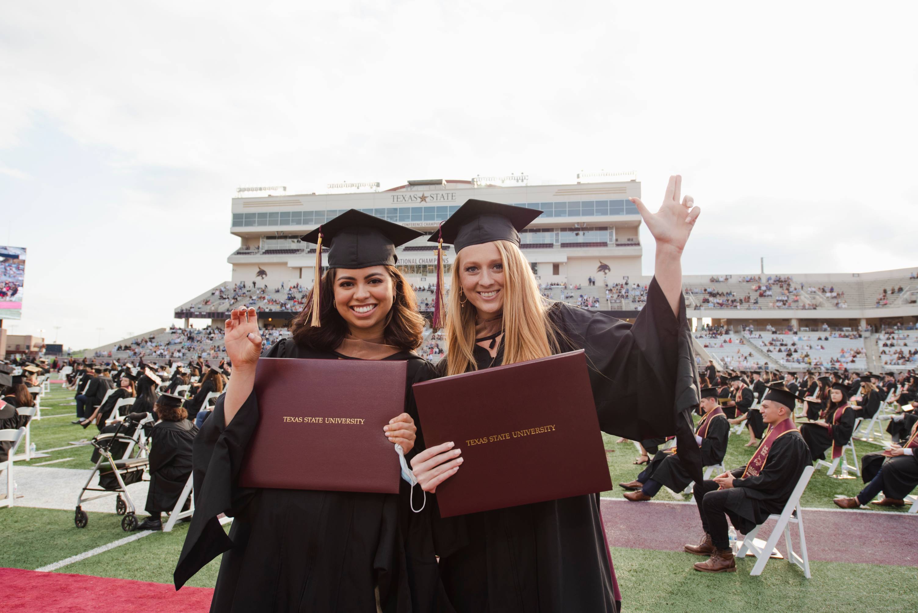 female graduates at commencement making TXST hand signs