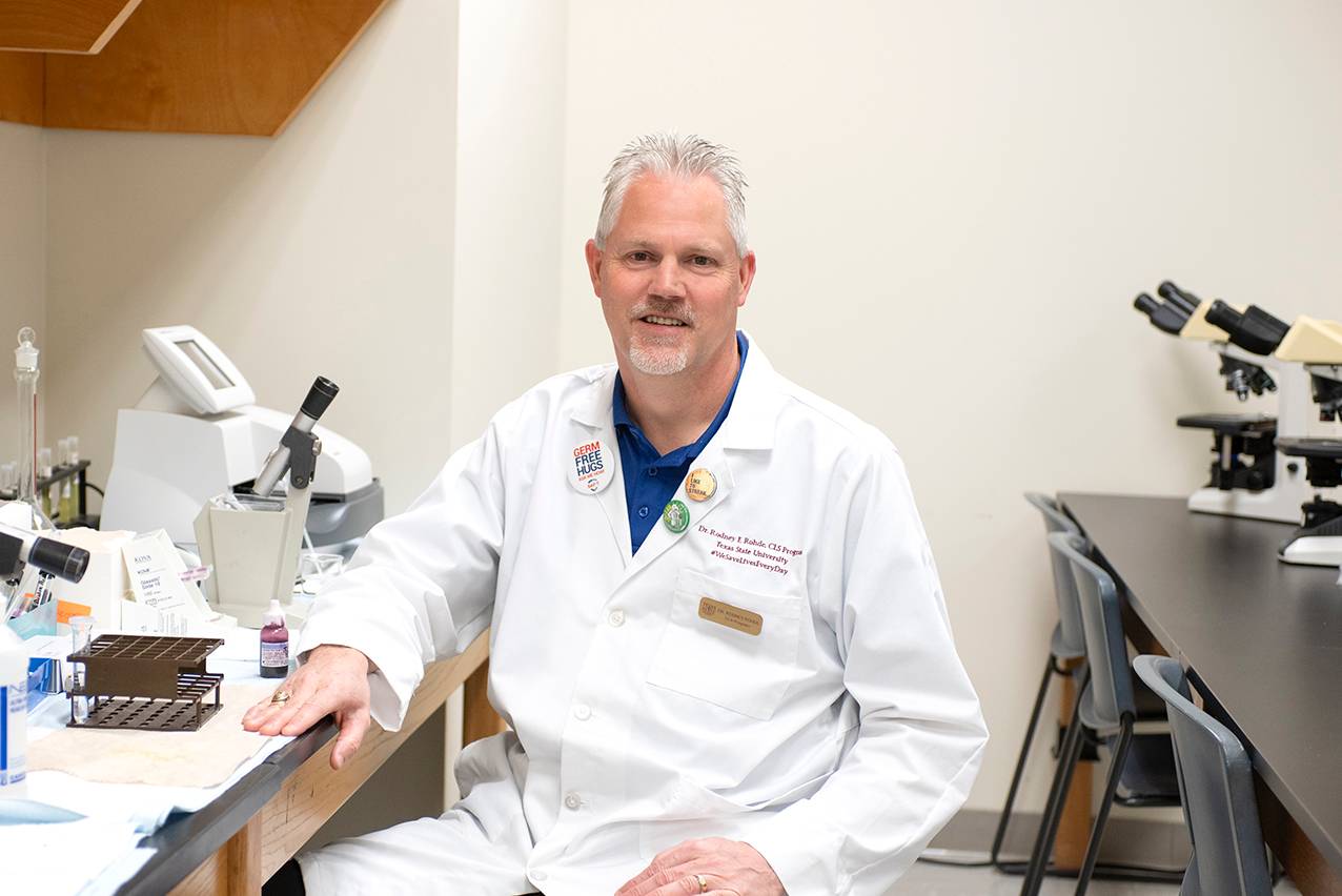 Rodney Rohde sits in a classroom in a labcoat.