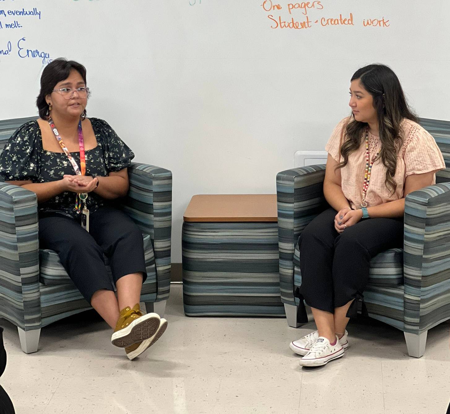 two females sitting in chairs in front of white board