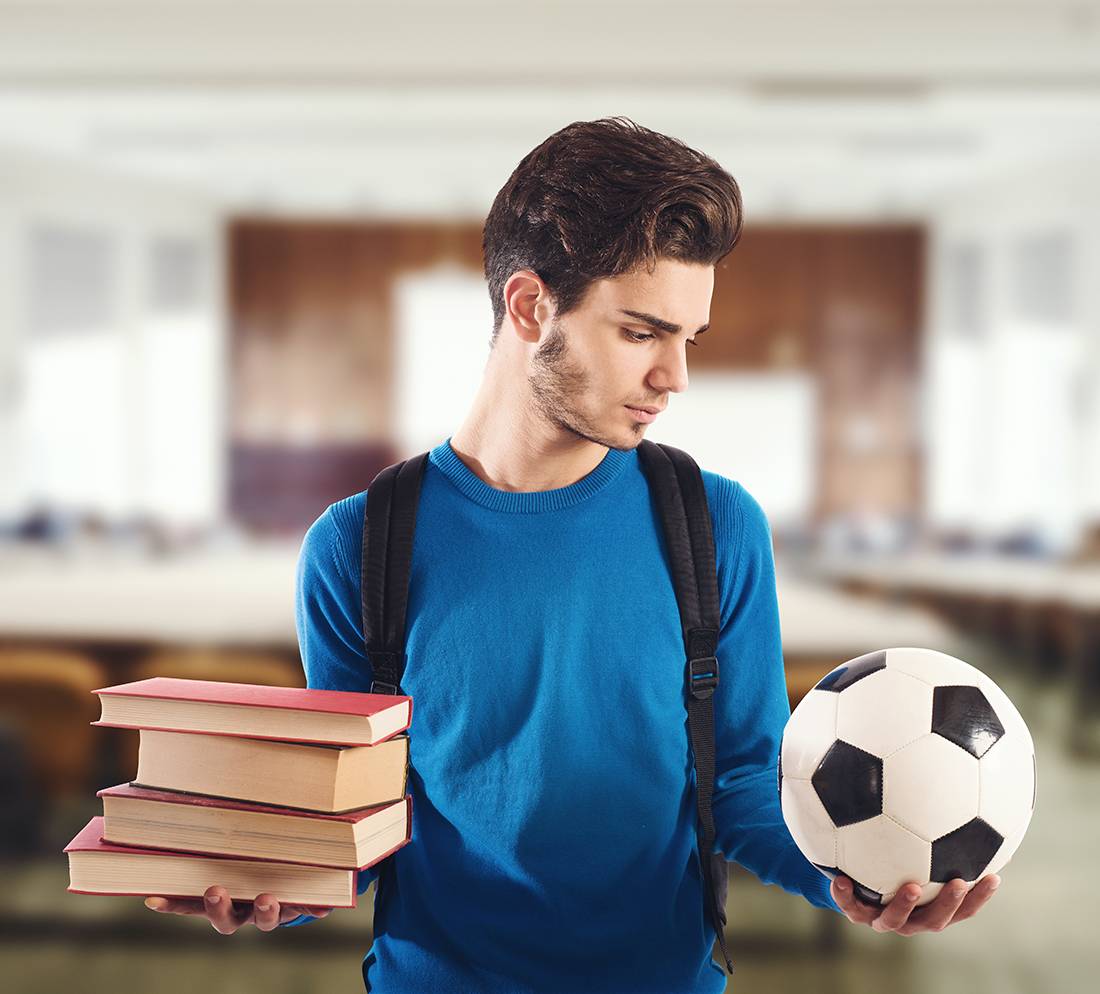 man holding soccer ball in one hand and school books in the other