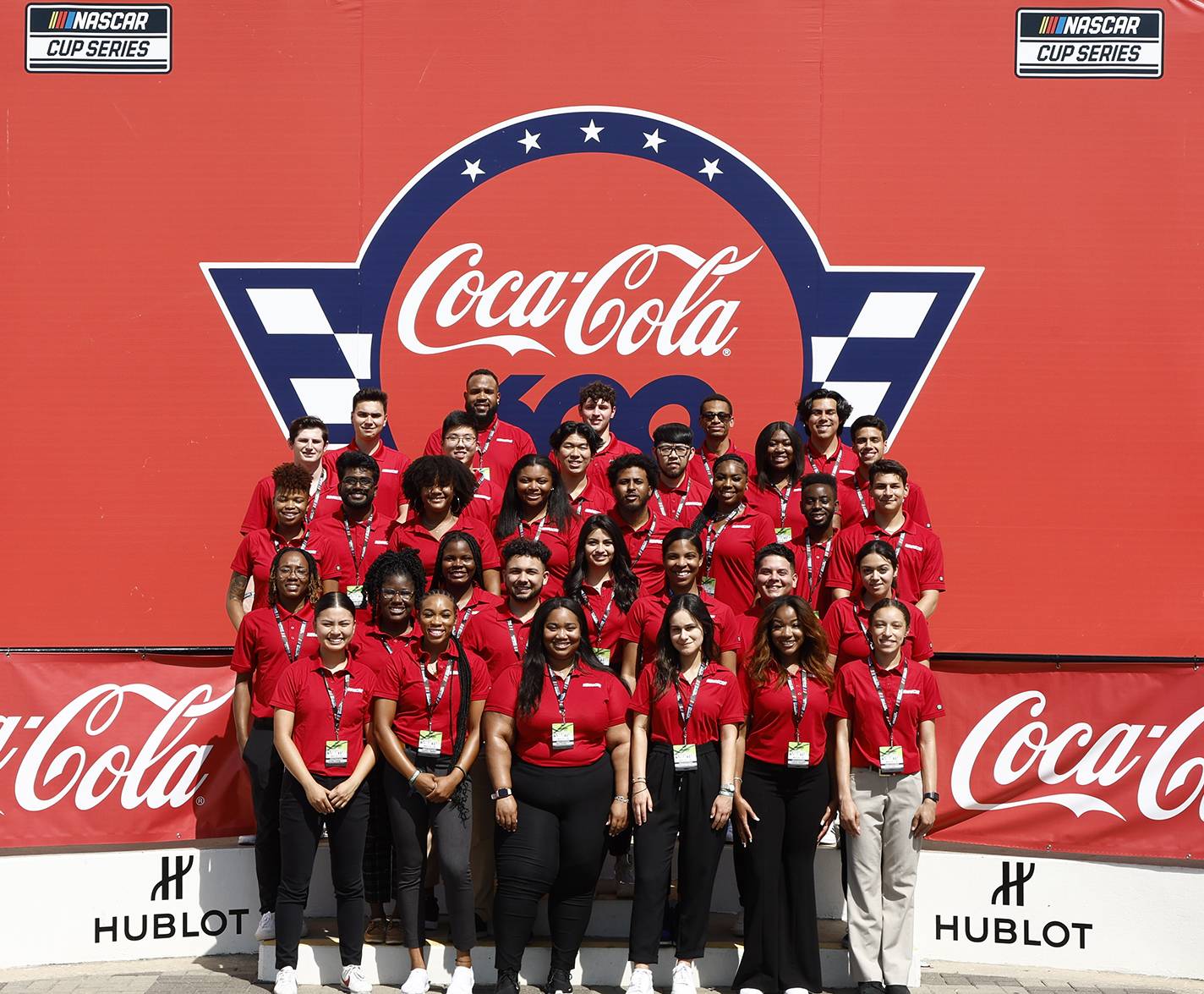 group of 36 students in front of red coca-cola wall