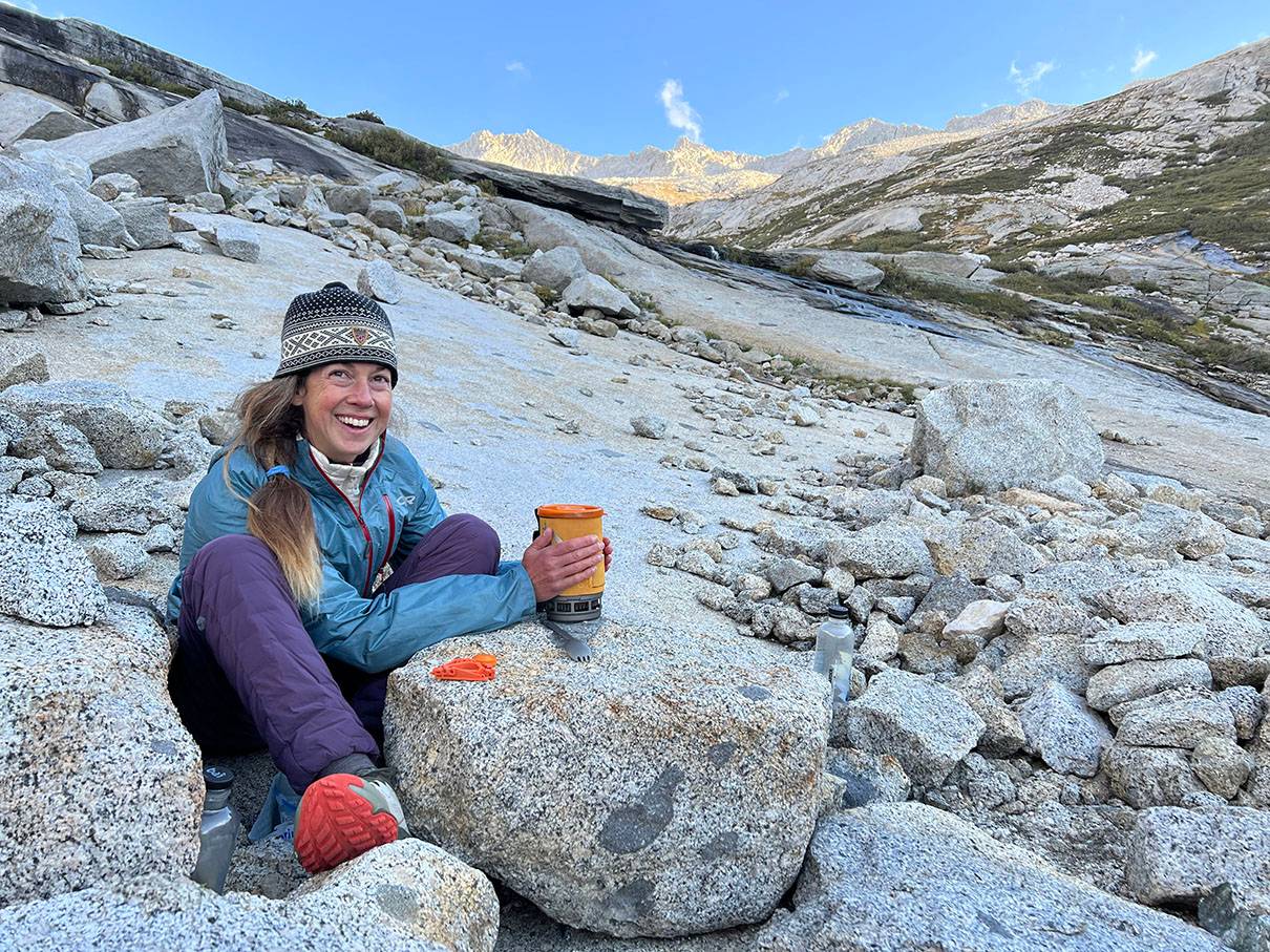 woman sitting on rocky mountain with cup in hands