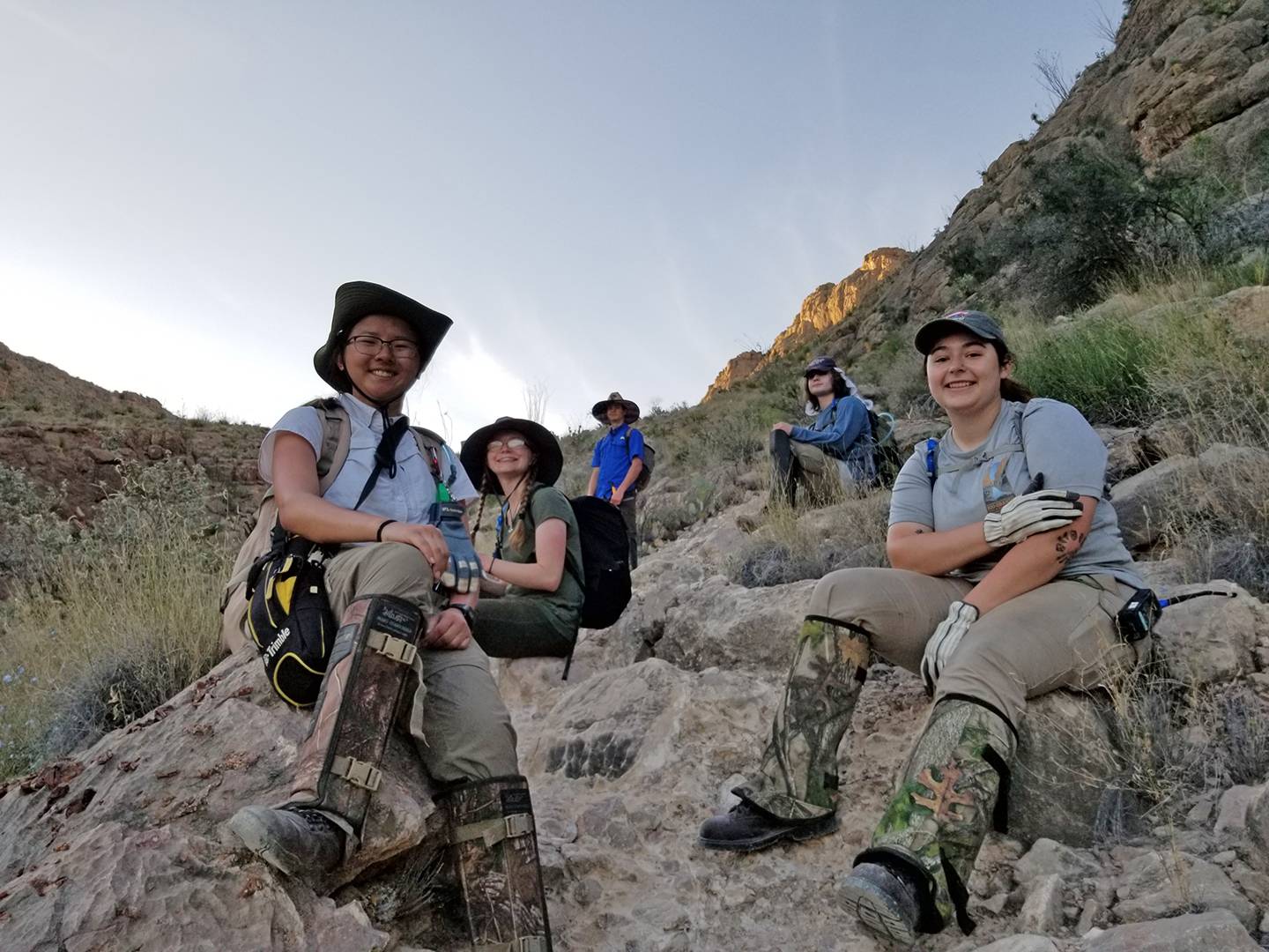 students smiling while sitting on rocks in mountain range