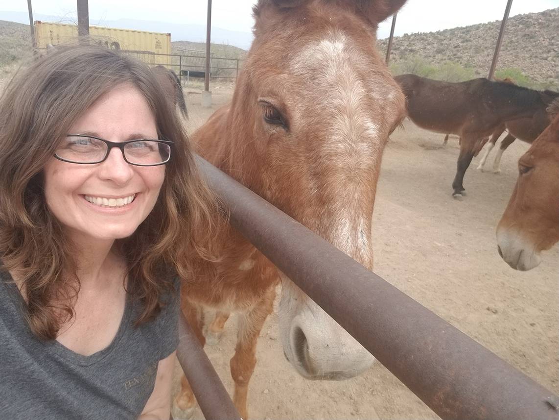 woman smiling next to brown horse
