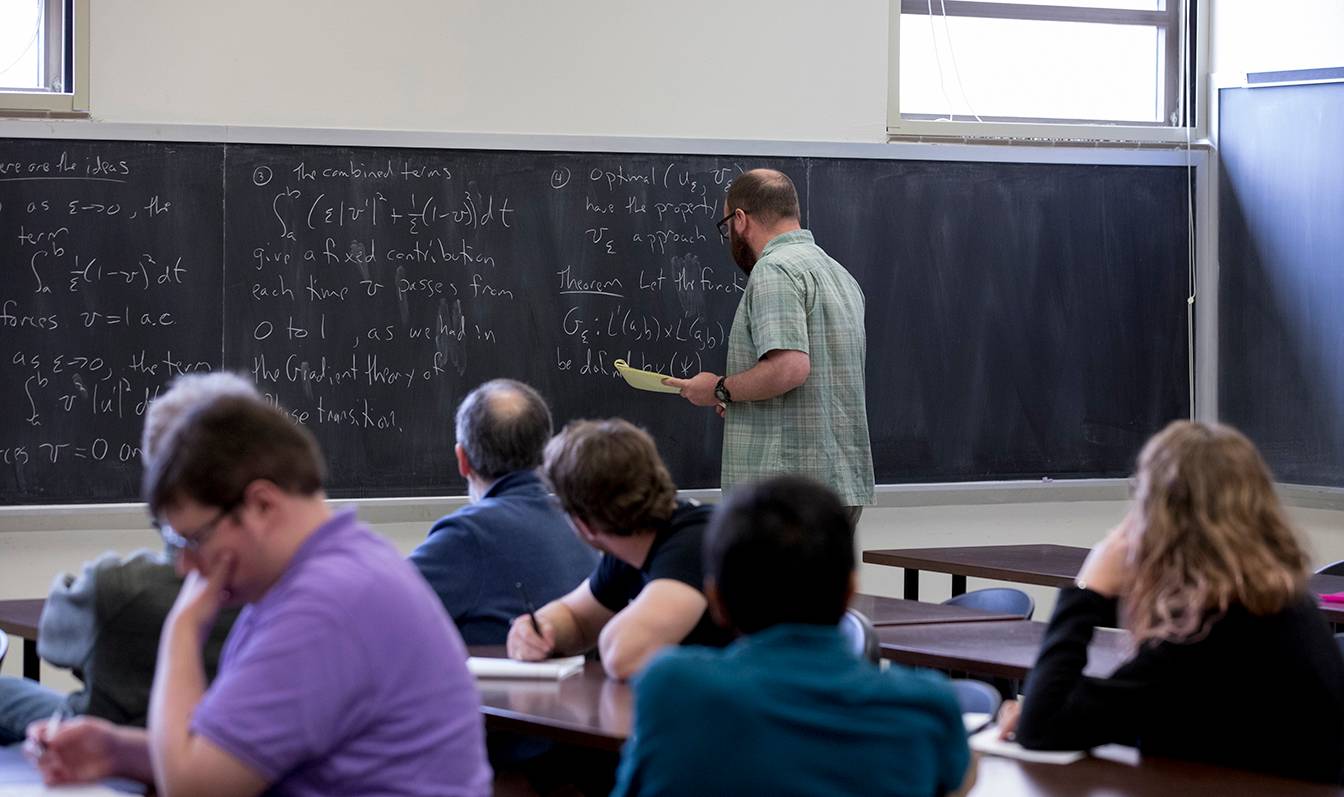 male math professor writing equations on chalk board