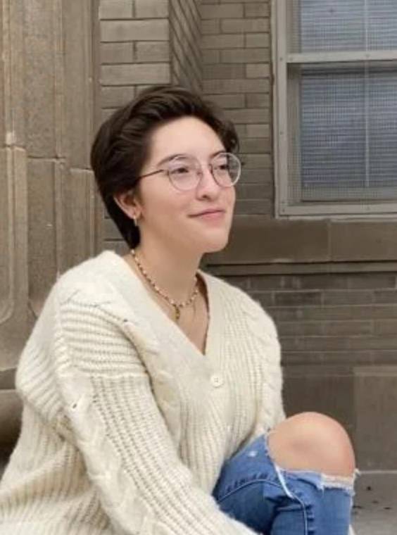 female student in white sweater sitting on step and looking off into the distance