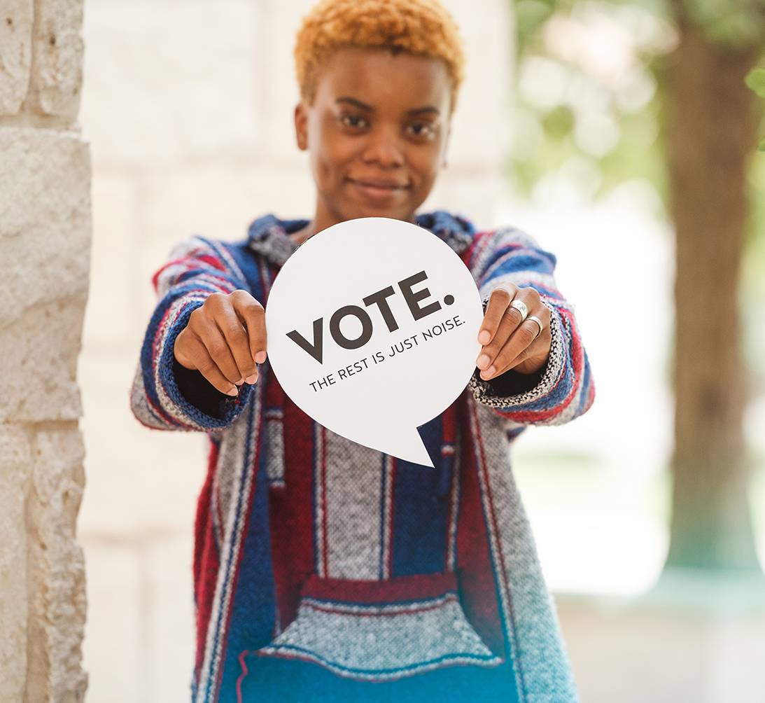 male student holding sign that reads "vote. the rest is just noise."