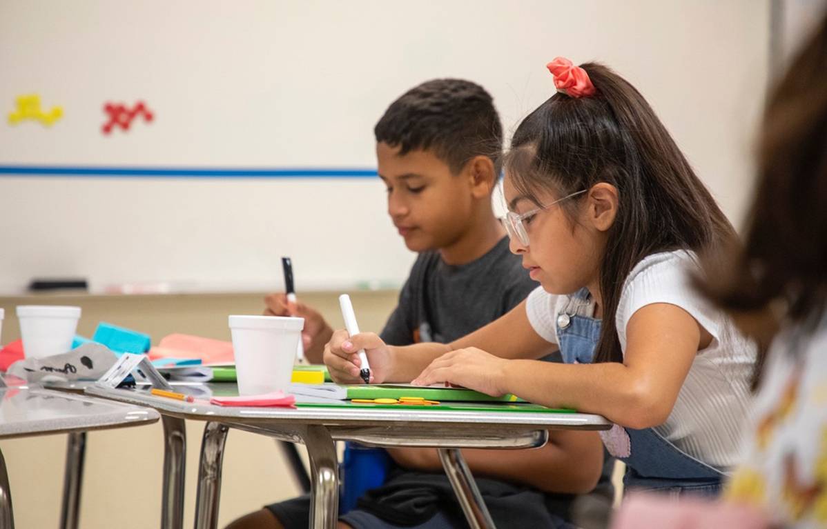 two young hispanic children writing in classroom setting