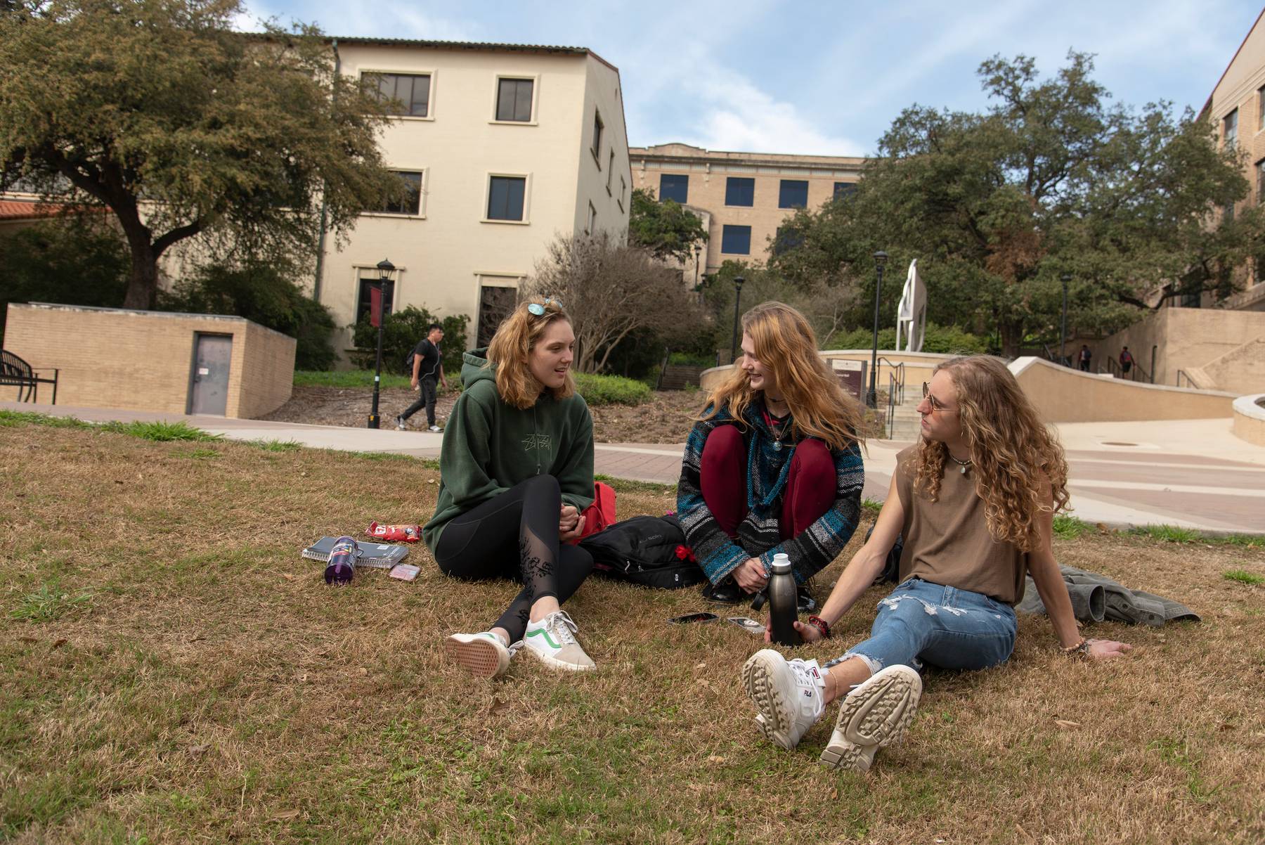 Three students sitting on the grass with blankets near east campus of Texas State University.