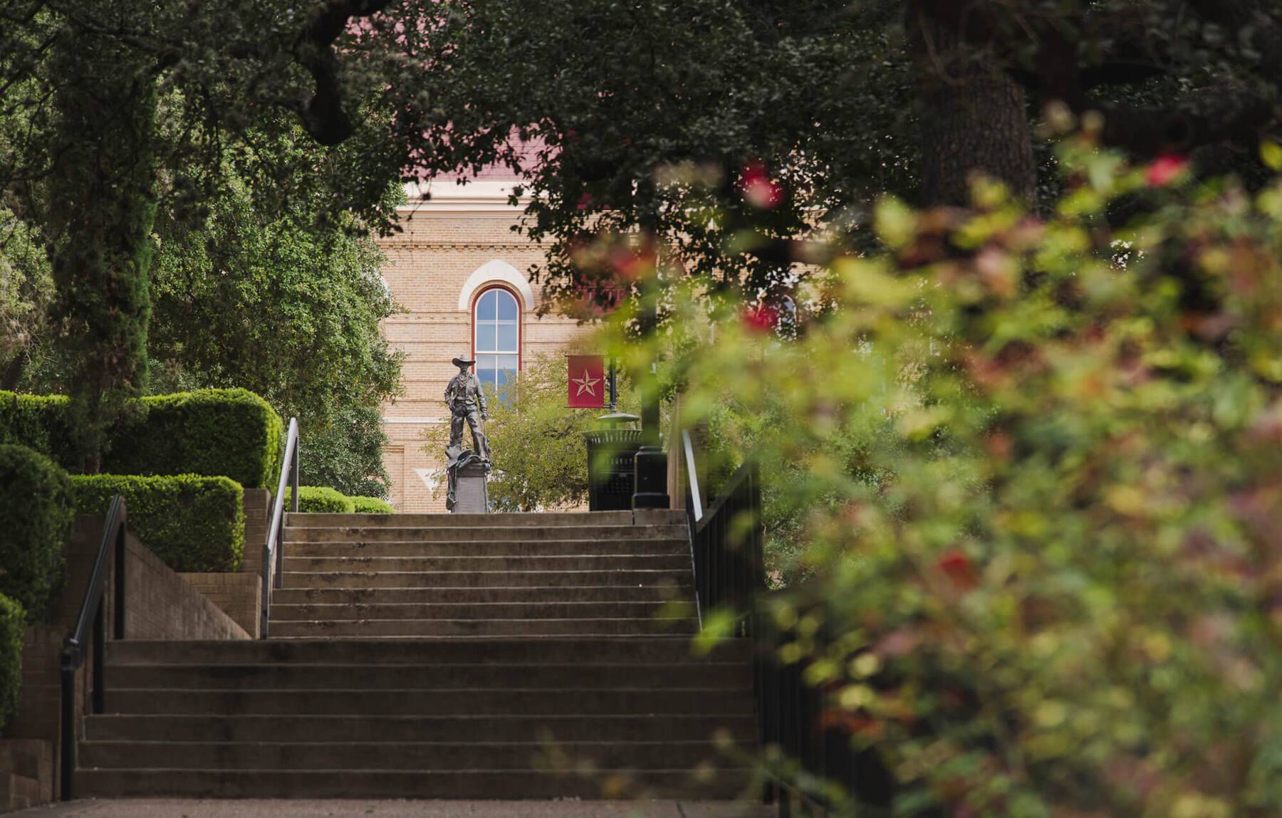 an exterior image of stairs leading up to old main with greenery and flowers blooming