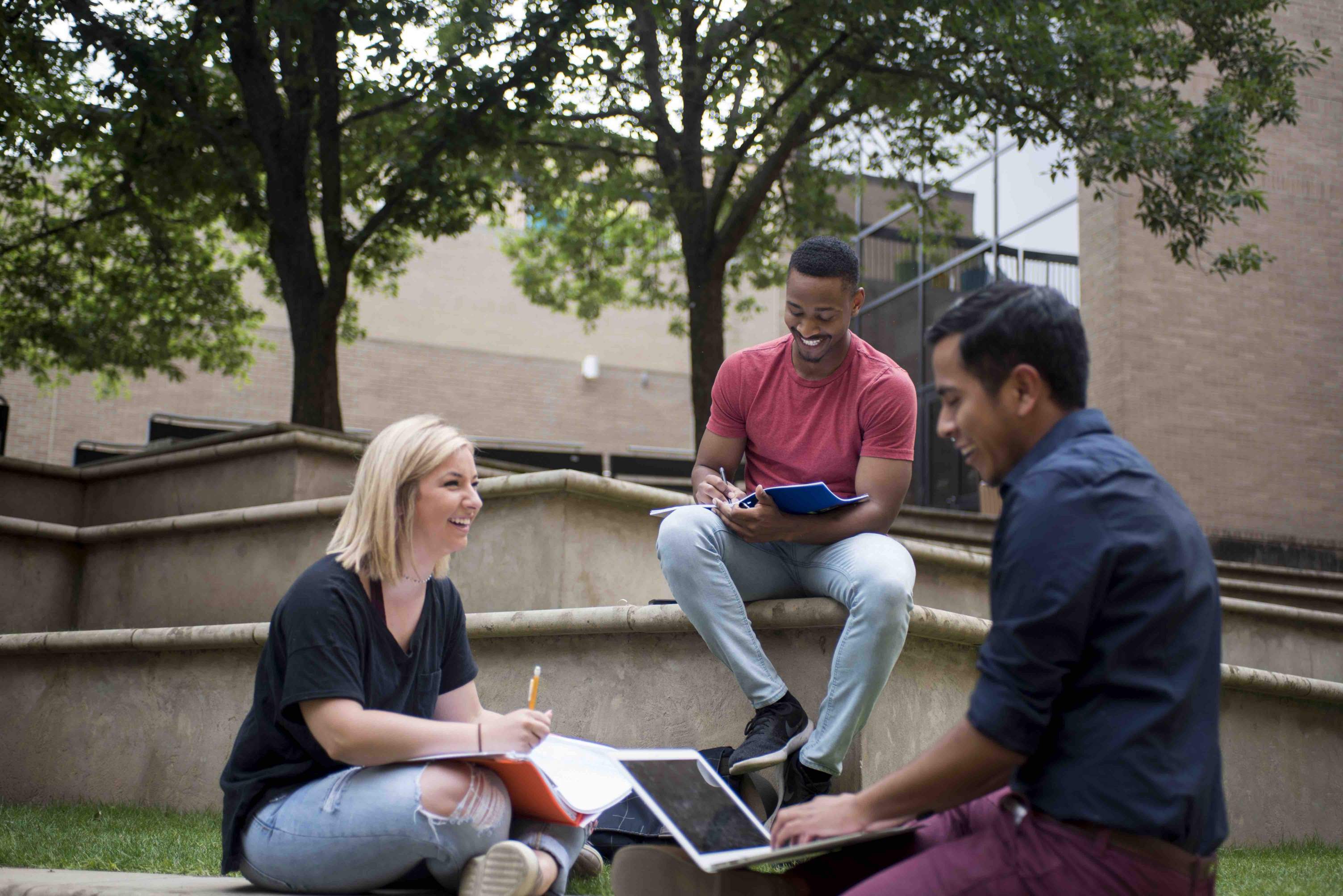 three students laughing and studying outside