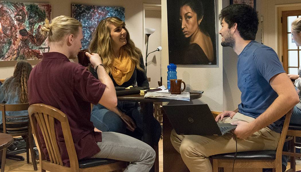 three students drink coffee and study at a table in the Honors College Coffee Forum
