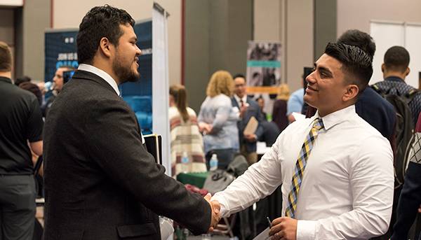 A student dressed in professional attire shakes hands with a potential employer