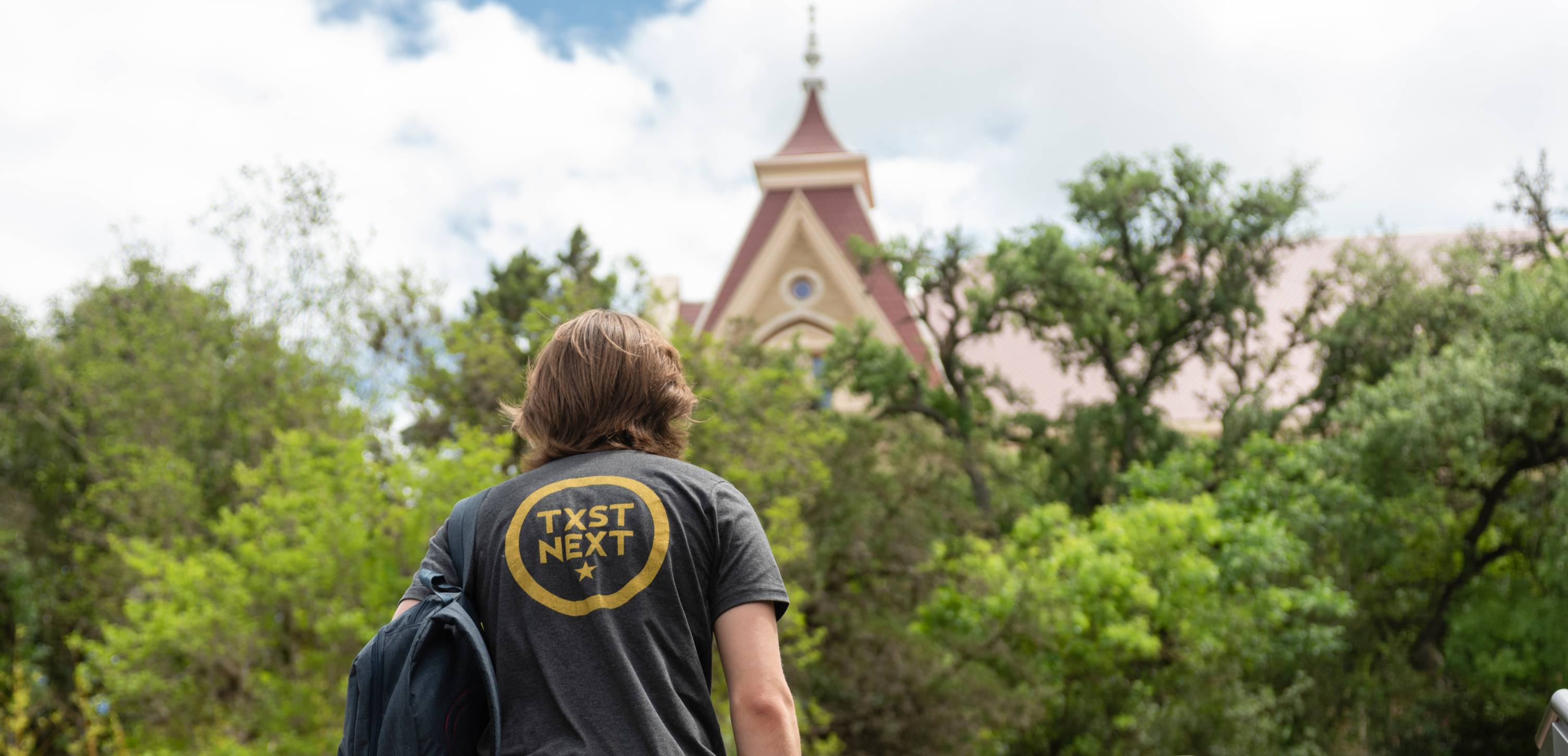 Male student with TXST NEXT t-shirt walking up to Old Main