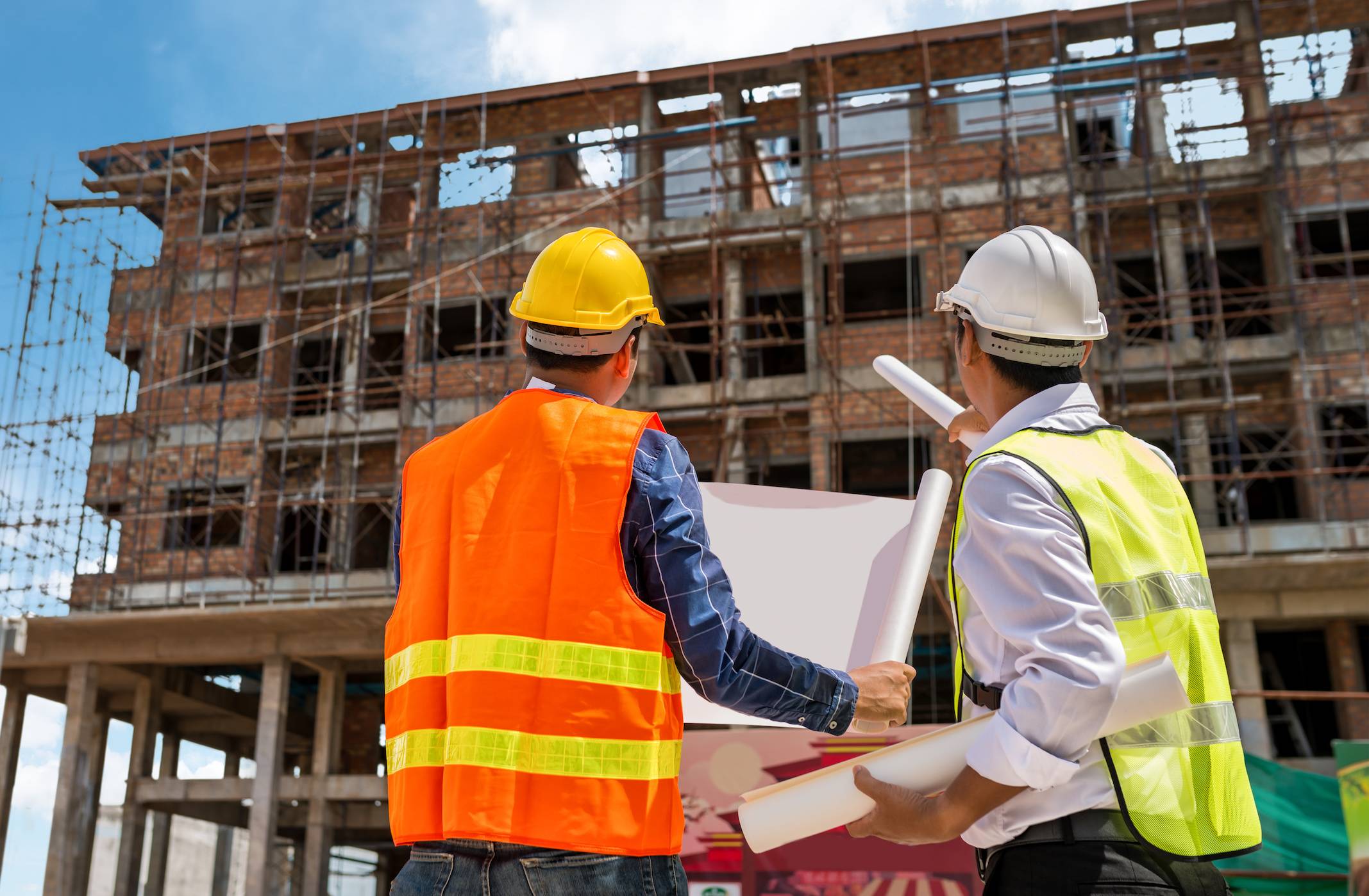 Construction workers holding building plans and overlooking a building construction site