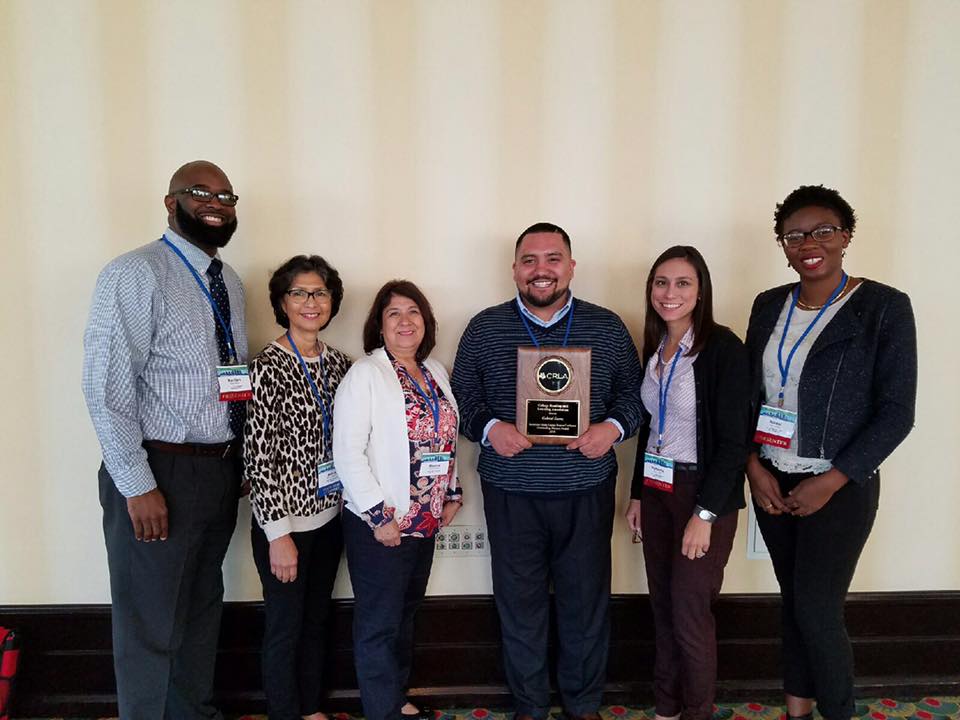 A peer mentor stands holding an award along with program staff.