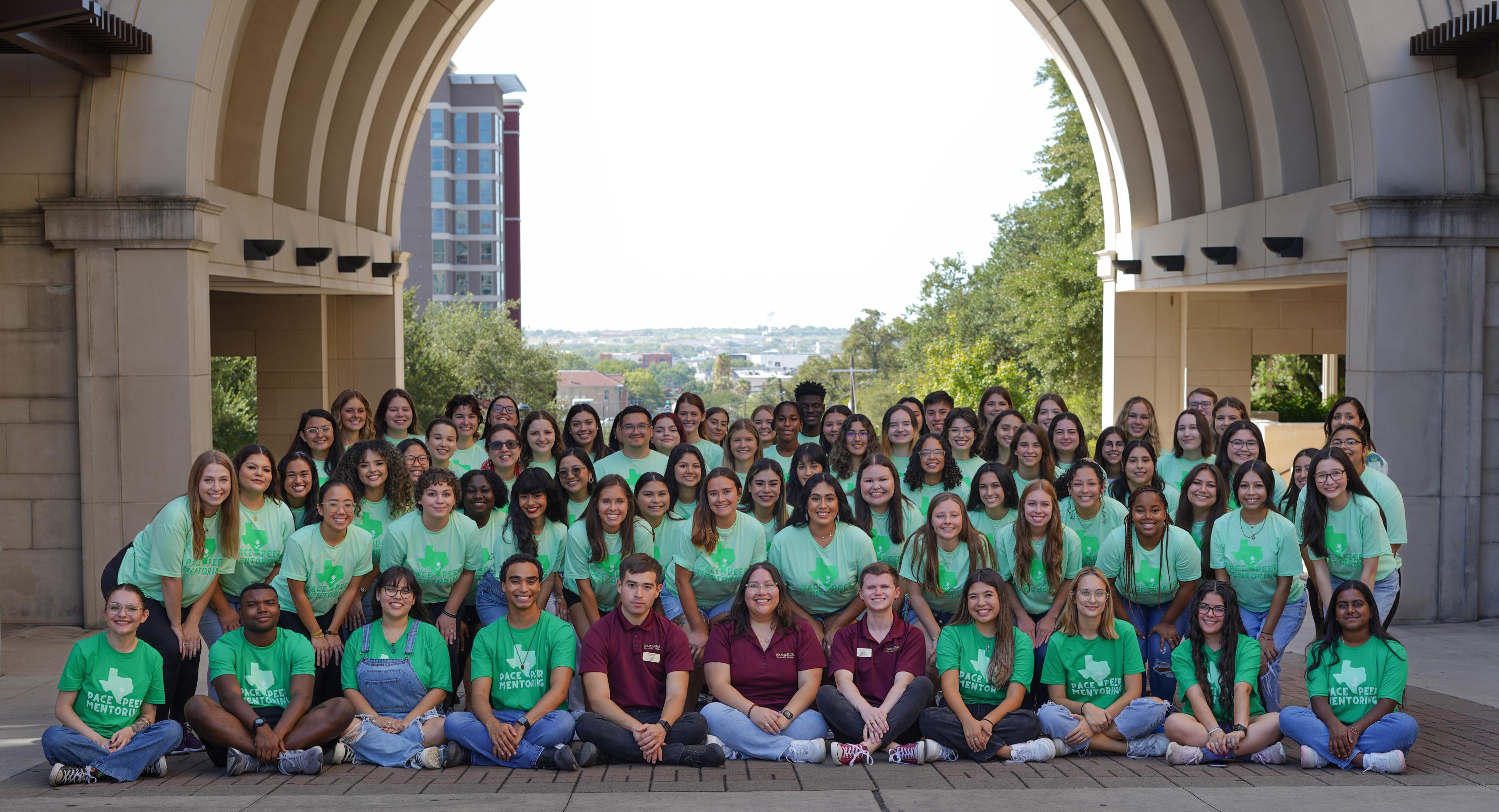 Peer mentors, graduate assistants, and program staff under the Trauth-Huffman Hall arch.