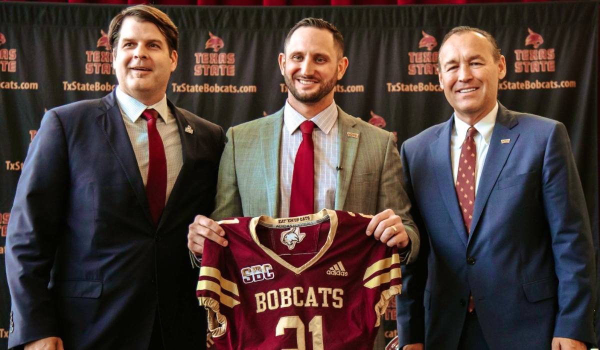 Don Coryell, GJ Kinne, and President Damphousse smiling while Kinne holds a bobcat jersey