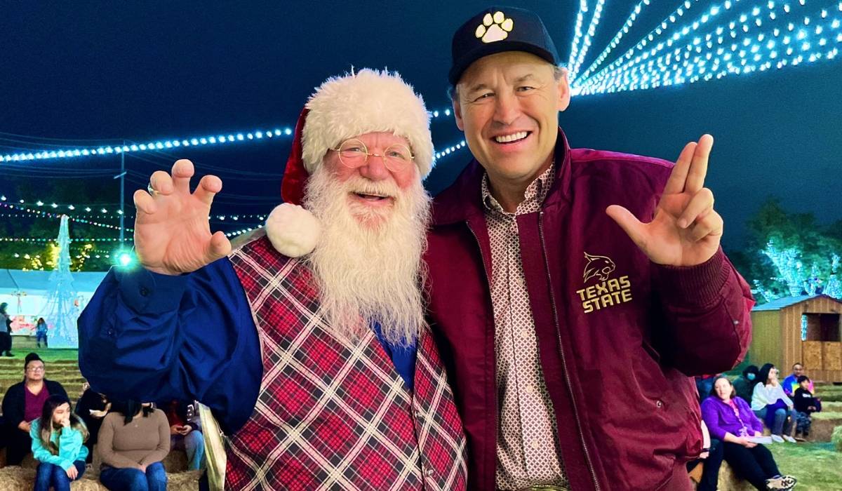 President Damphousse smiling and using the TXST hand signs with Santa