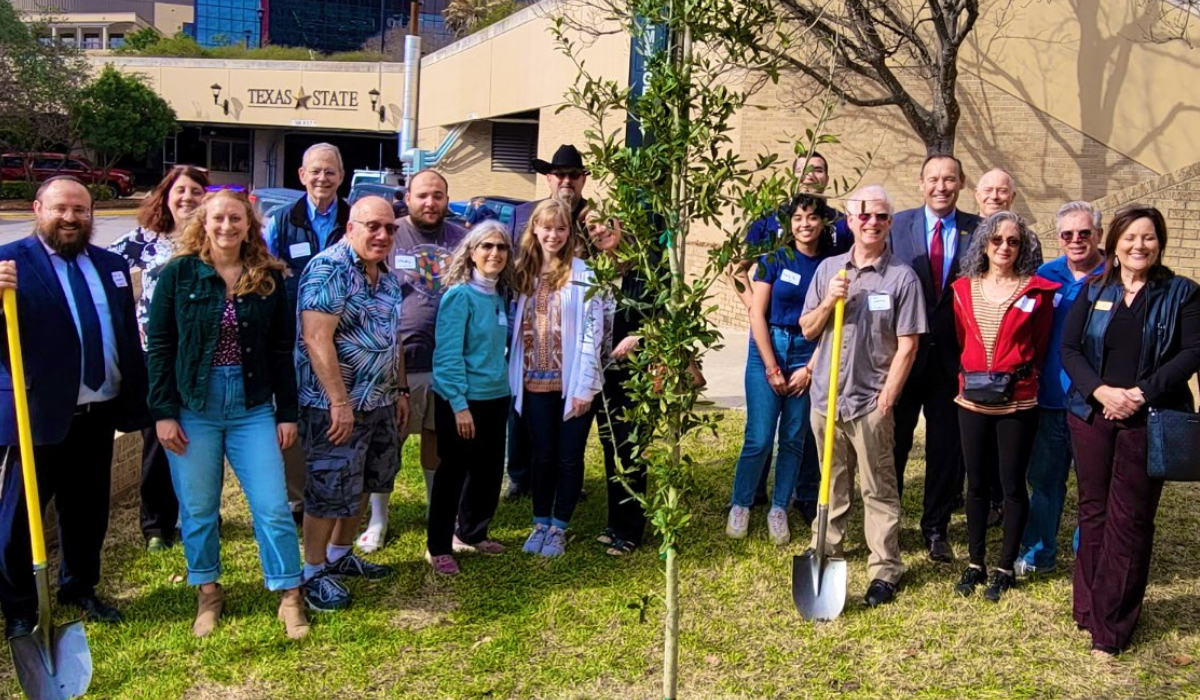 President Damphousse smiling with faculty and staff in front of a newly planted tree