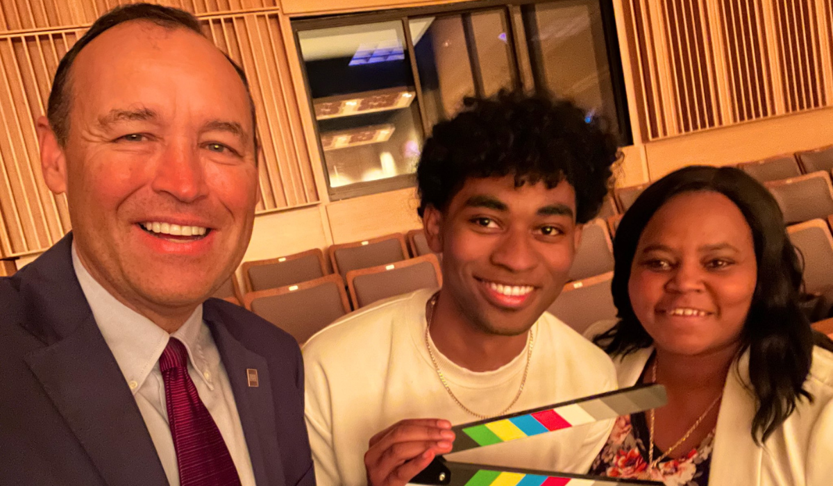 President Kelly Damphousse smiling with two students and a film marker