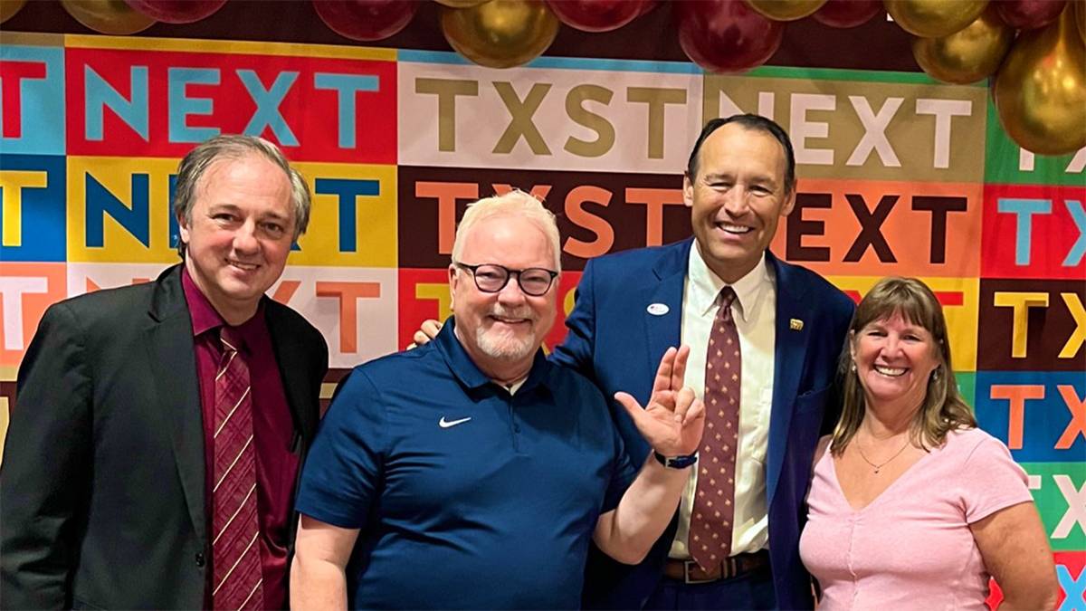 Dr. Damphousse, faculty, and staff stand in front of a colorful TXST NEXT banner.