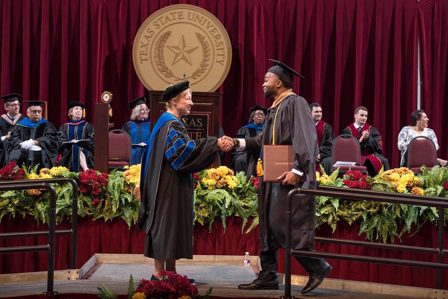 dr trauth shaking the hand of young man on stage during commencement