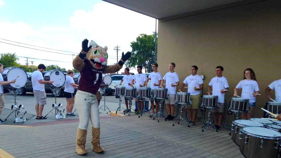 Boko the Bobcat directing the drumline in a parking lot.