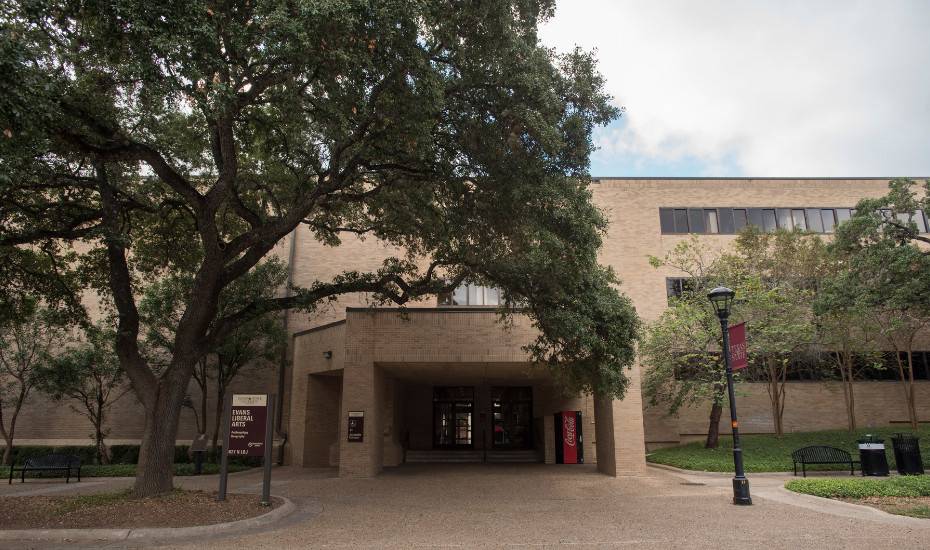 A brown brick building, with a brick walkway and tree in front.