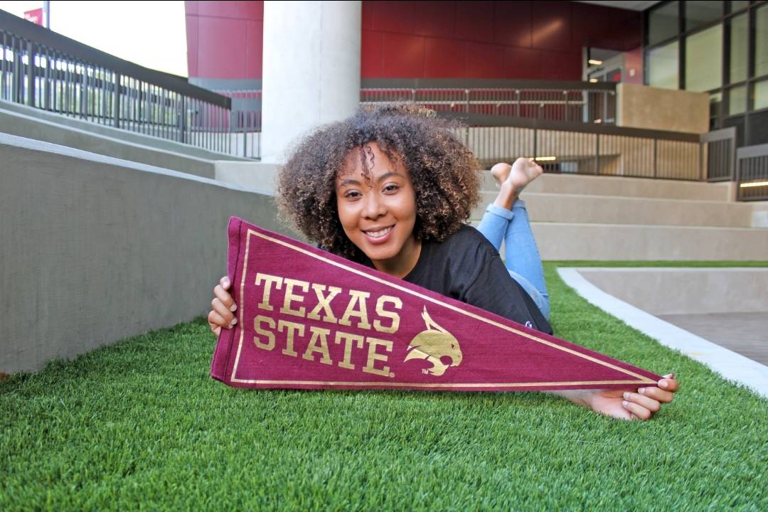Destiny McCalla poses with a TXST flag in the LBJ Student Center amphitheater.